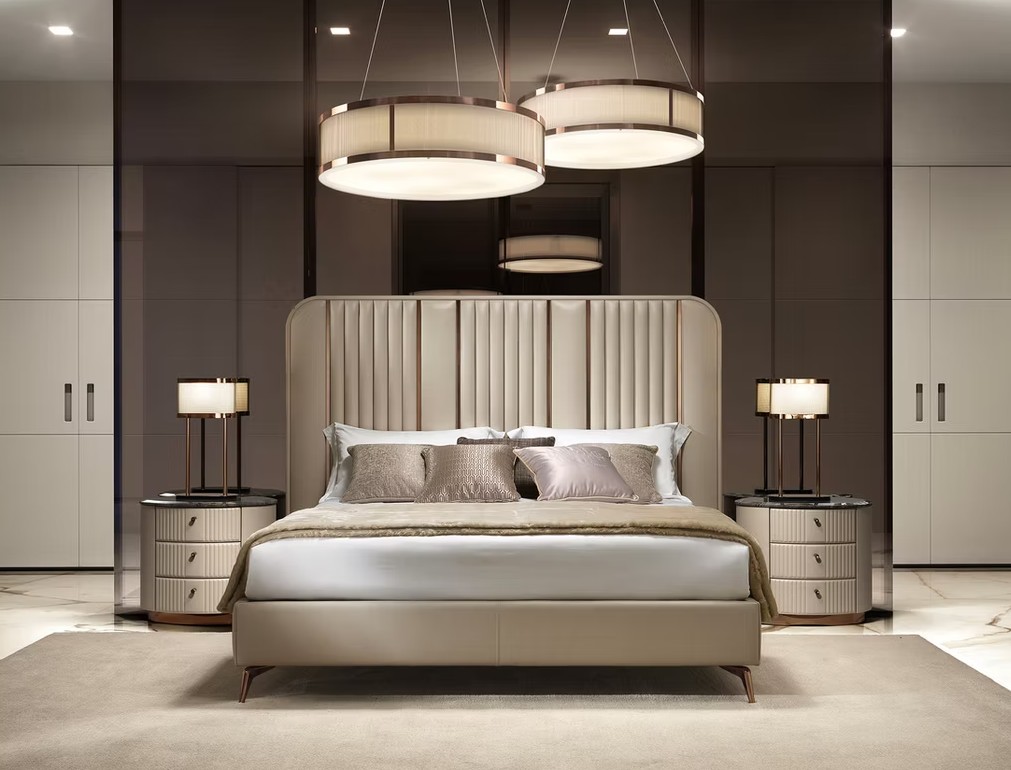 Luxurious beige upholstered bed with a tall padded headboard, matching nightstands, and warm pendant lights in a modern bedroom