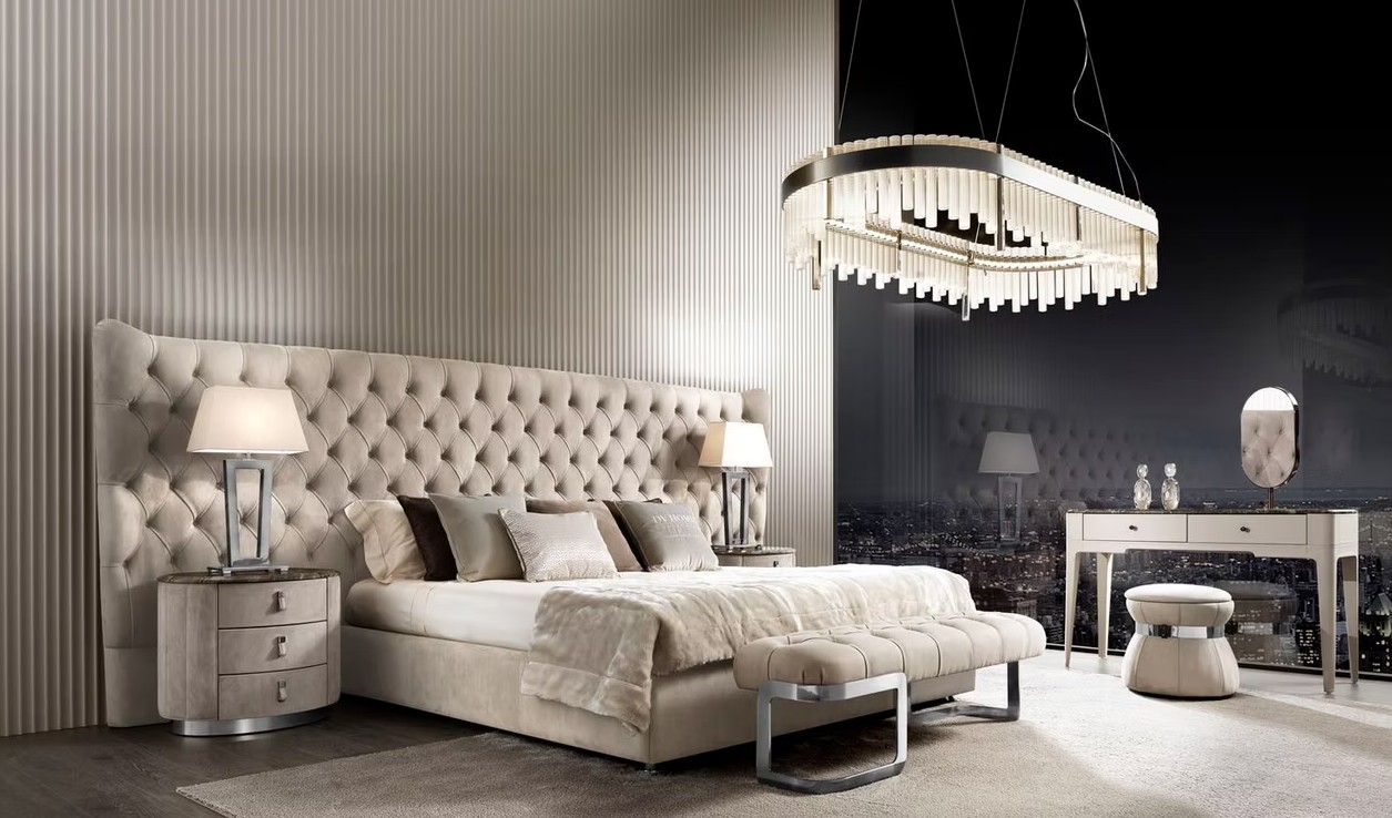 Hotel-style bedroom with a plush tufted beige headboard, matching nightstands, lamps, and a circular chandelier.