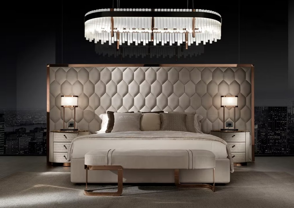 Luxurious bedroom with a tall tufted beige headboard, copper accents, and a crystal chandelier over the bed.